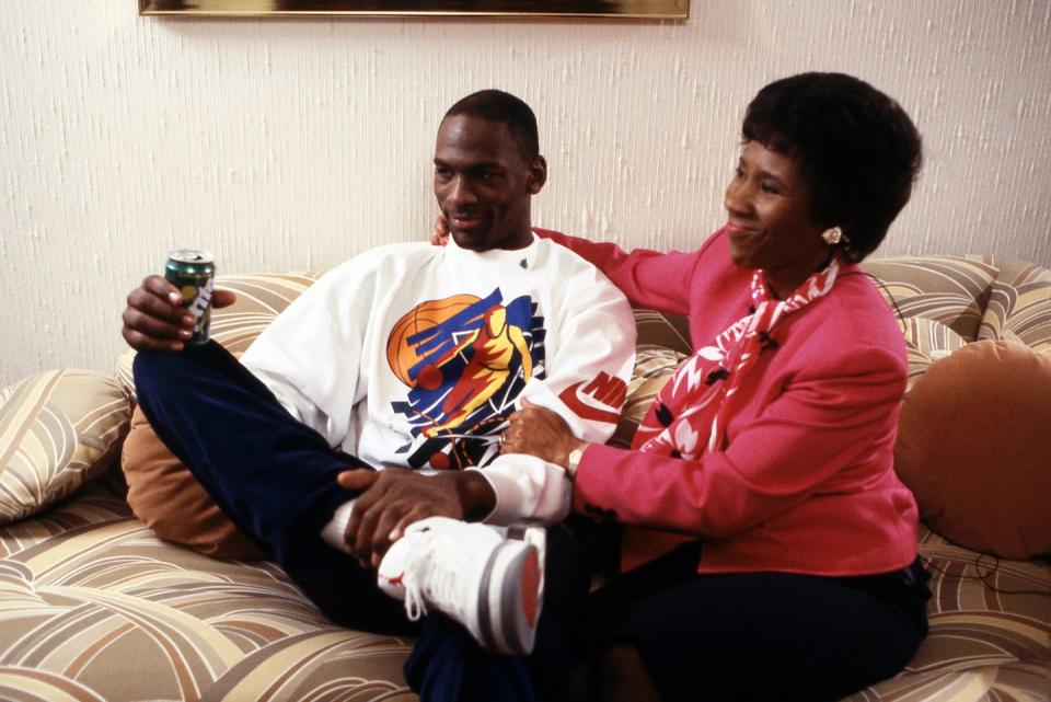 michael jordan, wearing a white sweatshirt with a basketball player on it, sitting on a couch next to deloris jordan, wearing a pink blouse