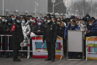 Security personnel stand watch as masked people gather in line for coronavirus testing in Beijing, Monday, Jan. 24, 2022. Chinese authorities have lifted a monthlong lockdown of Xi'an and its 13 million residents as infections subside ahead of the Winter Olympics. Meanwhile, the 2 million residents of one Beijing district are being tested following a series of cases in the capital. (AP Photo/Andy Wong)