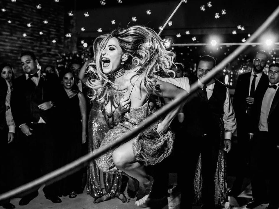 A black and white photo of a woman jumping over a rope in a party dress as people look on.