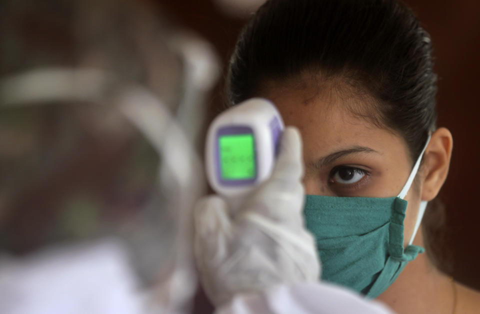 A health worker takes takes the temperature of a girl at a residential building in Mumbai, India, Wednesday, July 22, 2020. With a surge in coronavirus cases in the past few weeks, state governments in India have been ordering focused lockdowns in high-risk areas to slow down the spread of infections. (AP Photo/Rafiq Maqbool)