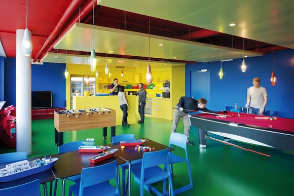Workers relaxing in a brightly colored break room in Google's primary colors, featuring a pool table and some foosball action.