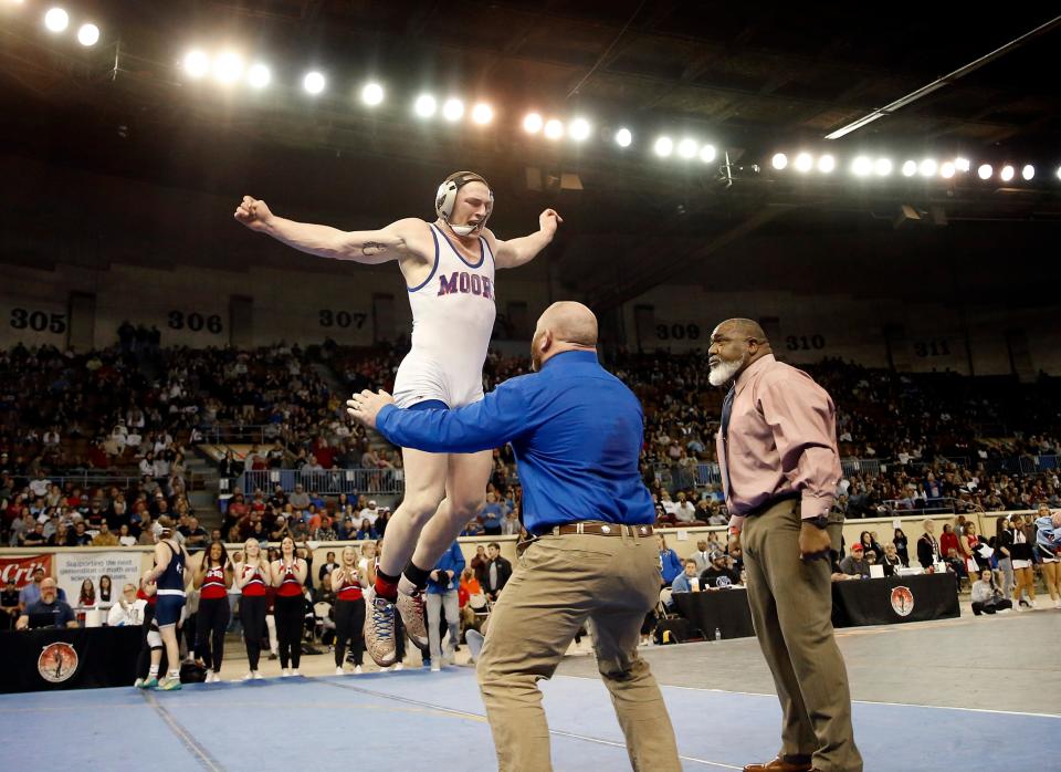 Moore's Payton Thomas leaps and celebrates with his dad and coach, Tim Thomas, as head coach Robert Washington looks on. Thomas beat Stillwater's AJ Heeg in the Class 6A 190-pound match during the state wrestling tournament finals Saturday at State Fair Arena.