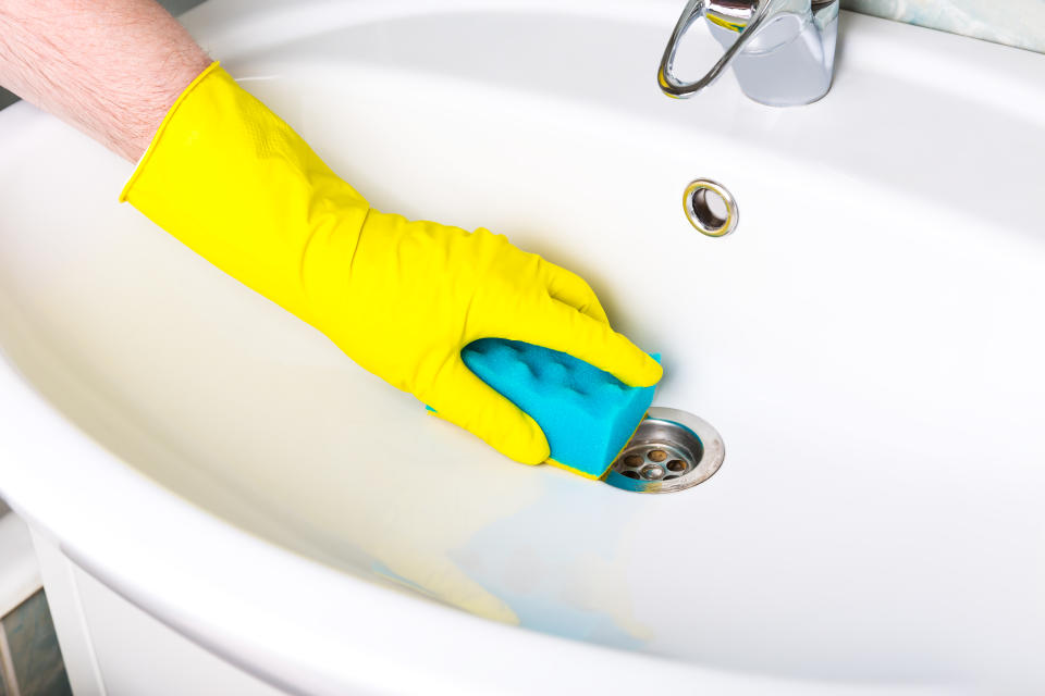 Pandemic disinfection. Man in yellow gloves cleans bathroom tap and the bath and sink. Maid in yellow protective gloves washing dirty bath tap or sink. Hands of man wash or cleans up bath. Close-up.