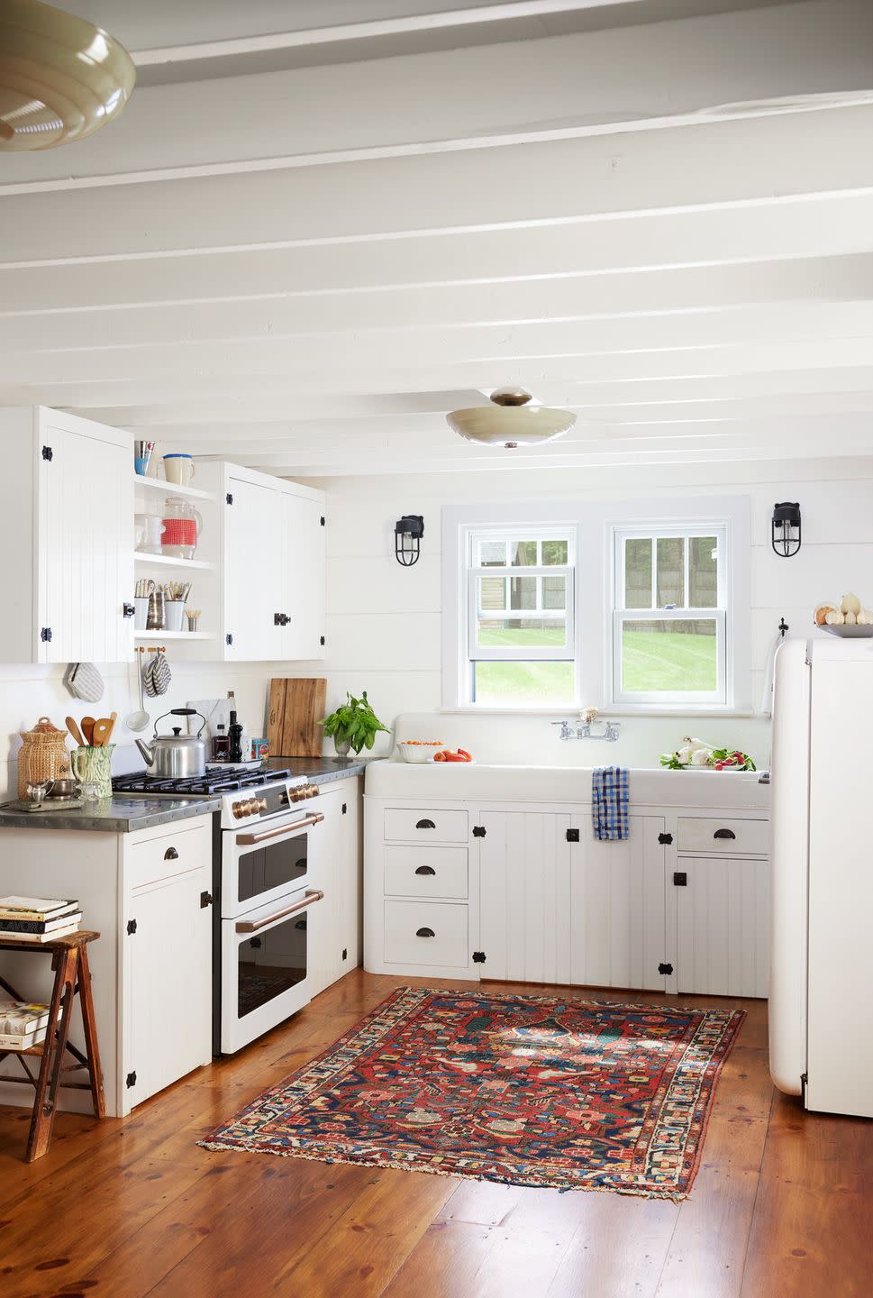 an all white corner kitchen with a colorful vintage rug over hardwood floors