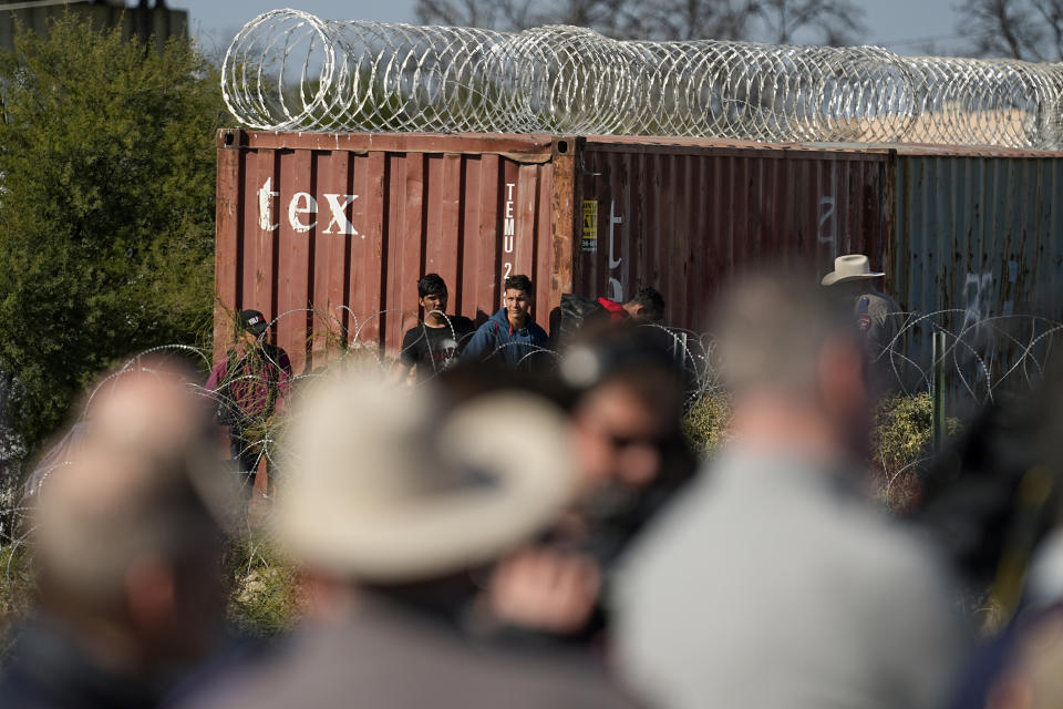 Members of Congress, bottom, look on as as migrants walk near a rail car covered in Concertina wire at the Texas-Mexico border, Wednesday, Jan. 3, 2024, in Eagle Pass, Texas. U.S. House Speaker Mike Johnson is leading about 60 fellow Republicans in Congress on a visit to the Mexican border. Their trip comes as they are demanding hard-line immigration policies in exchange for backing President Joe Biden's emergency wartime funding request for Ukraine. (AP Photo/Eric Gay)