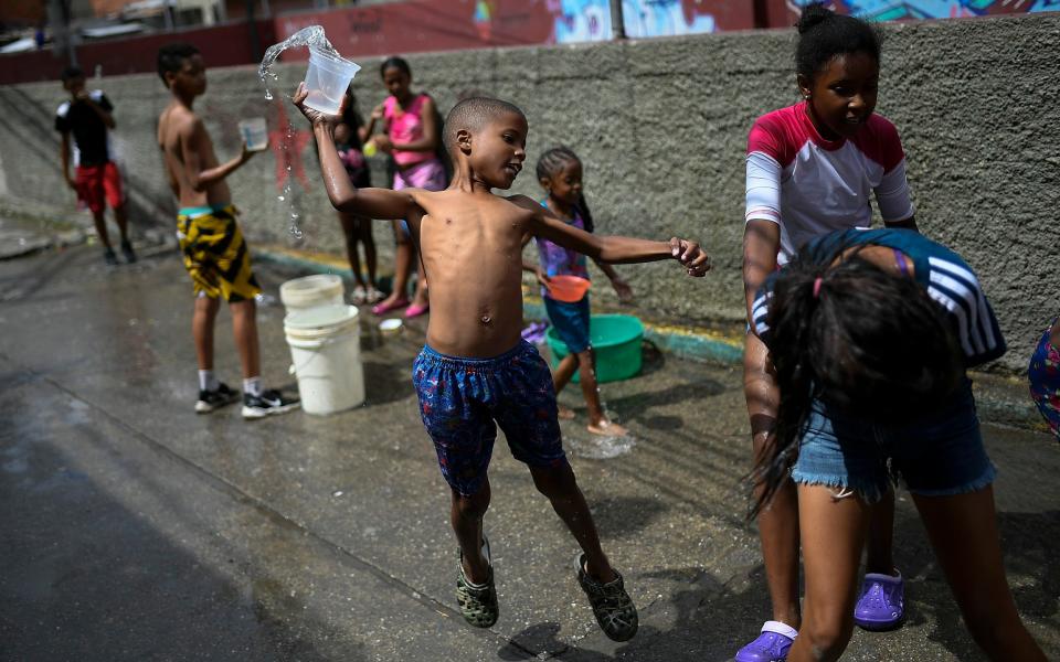 A boy prepares to playfully drench a friend with water during carnival celebrations in the Pinto Salinas neighborhood of Caracas, Venezuela - AP