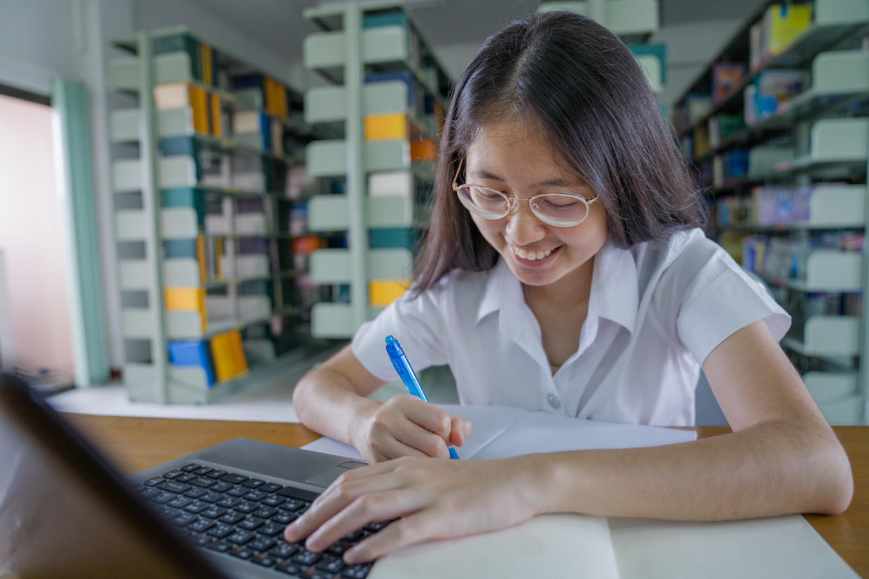 An asian girl in an education facility, likely a library, doing her homework.