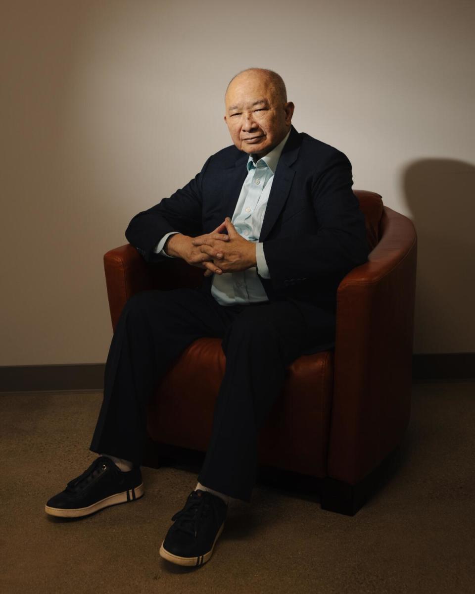 A man in a blazer and sneakers sits for the camera.