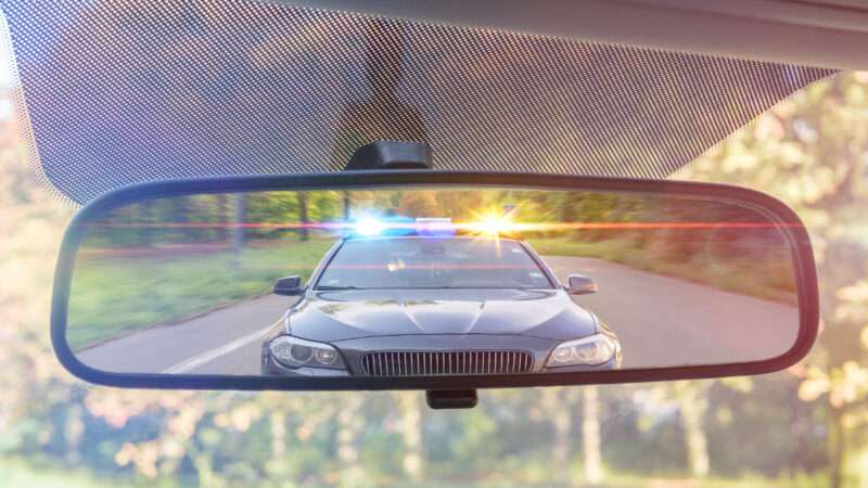 Police with flashing lights seen through a rearview mirror.