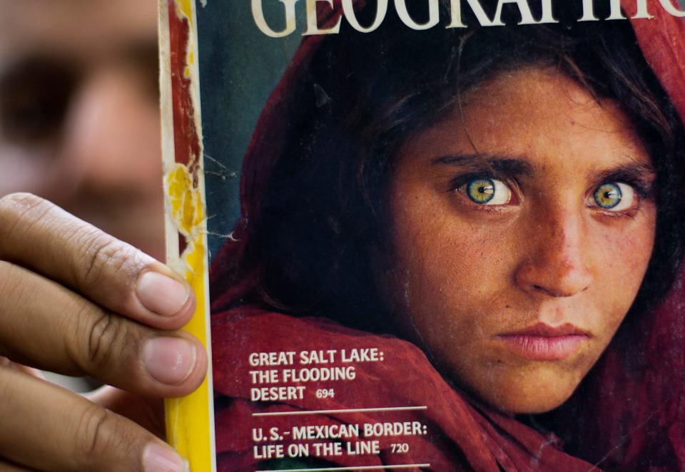 In this file photo taken on Oct. 26, 2016, Pakistan's Inam Khan, owner of a book shop shows a copy of a magazine with the photograph of Afghan refugee woman Sharbat Gulla, from his rare collection in Islamabad, Pakistan. National Geographic’s famed green-eyed “Afghan Girl” has arrived in Italy as part of the West’s evacuation of Afghans following the Taliban takeover of the country, the Italian government said Thursday.