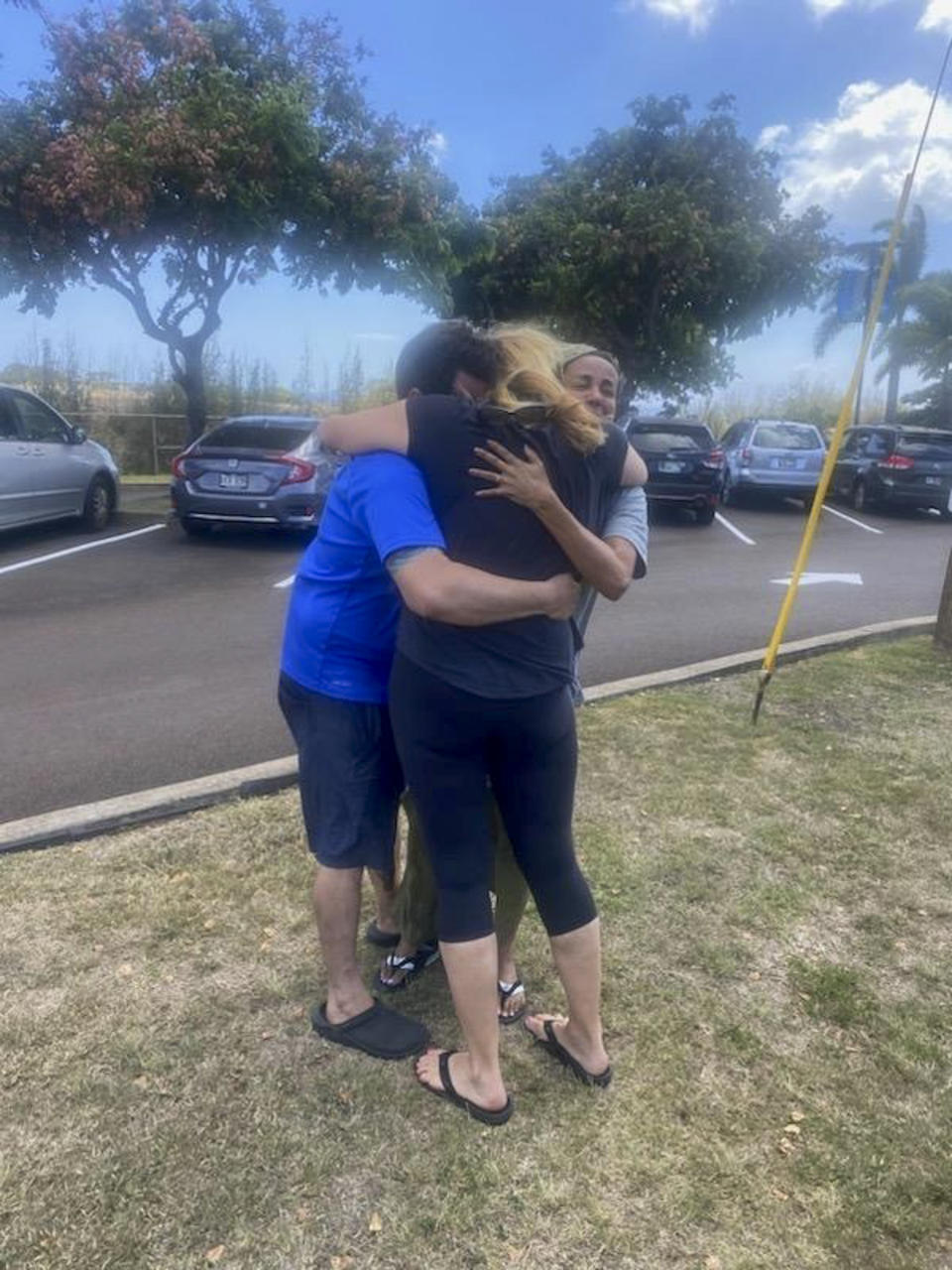 This Aug. 9, 2023 photo taken by his stepfather Mike Eilers and provided by Mike Cicchino shows Mike Cicchino, left, and his wife Andreza, right, hugs Mike's mother Susan Ramos as they were reunited at shelter in Maui, Hawaii. (Mike Cicchino via AP)