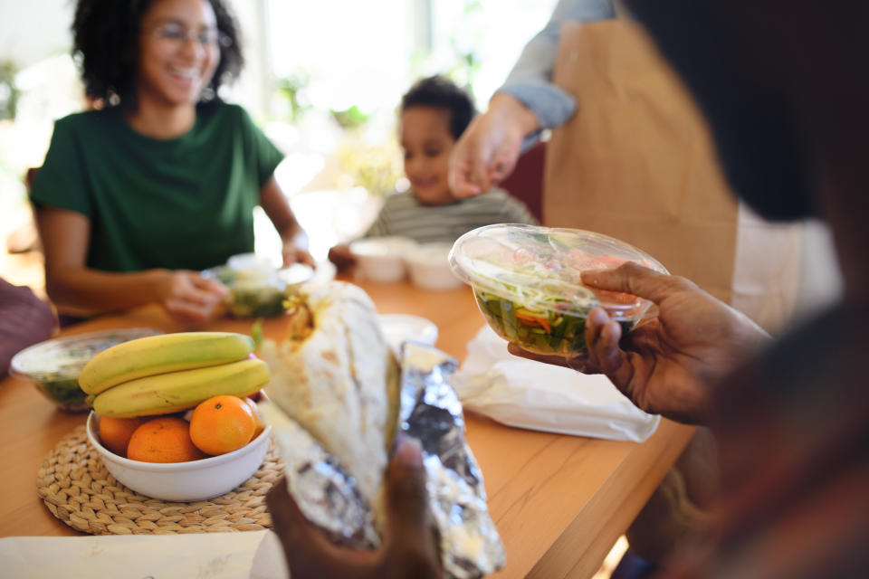 Family sitting at table and opening takeaway food together, featuring a burrito. (Getty Images)