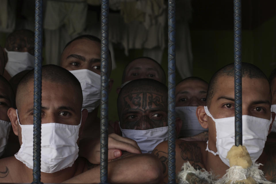 Imprisoned gang members, wearing protective face masks, look out from behind bars during a media tour of the prison in Quezaltepeque, El Salvador, Friday, Sept. 4, 2020. President Nayib Bukele denied a report Friday that his government has been negotiating with one of the country’s most powerful gangs to lower the murder rate and win their support in mid-term elections in exchange for prison privileges. (AP Photo/Salvador Melendez)