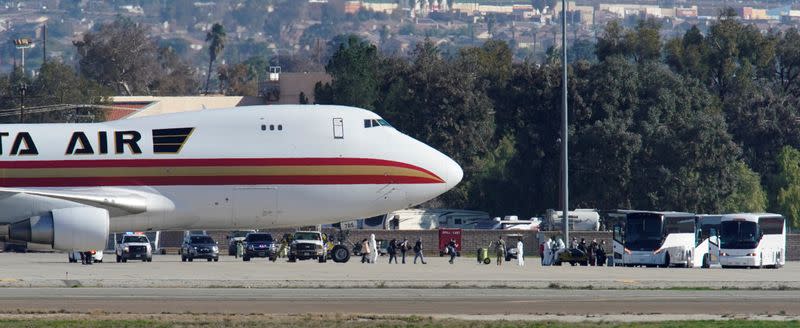 FILE PHOTO: Passengers board buses past personnel in protective clothing after arriving on an aircraft at March Air Reserve Base in Riverside County