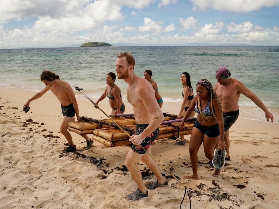 survivor players carrying a bamboo raft up the shore