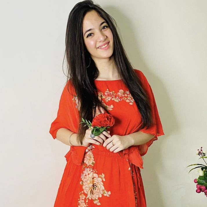 Siya is seen holding a red flower while smiling.