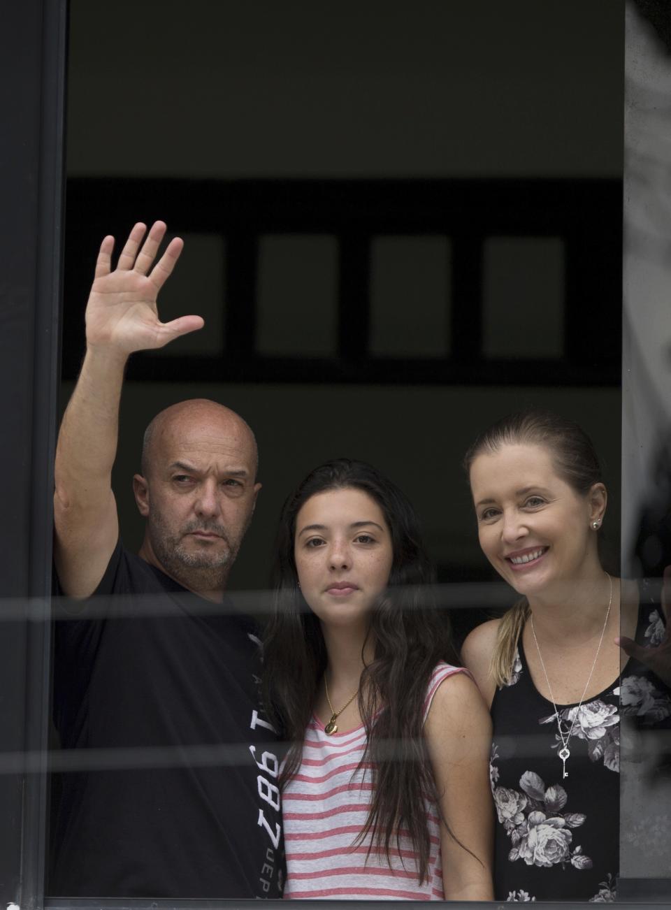 FILE - In this Sept. 20, 2014 file photo, Ivan Simonovis, former Caracas police chief, waves to the media from the balcony of his home, accompanied by his daughter Ivana, center, and wife Bony, in Caracas, Venezuela, after he was released from jail on humanitarian grounds to continue serving a 30-year sentence at home. Simonovis had been jailed since 2004 in connection with the death of pro-government protesters who had rushed to the defense of then-President Hugo Chavez during a failed coup attempt two years earlier. In 2009, he was convicted of aggravated murder. (AP Photo/Fernando Llano, File)