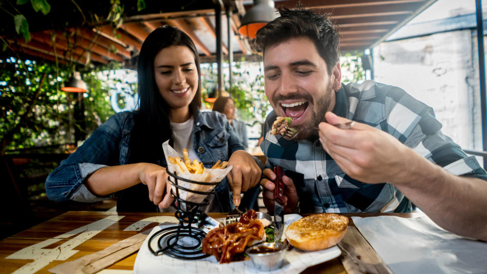 Loving couple eating together at a burgerâ??s restaurant and looking happy on a date.