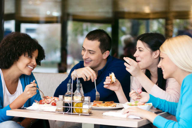 Four cheerful friends chatting while lunch in restaurant