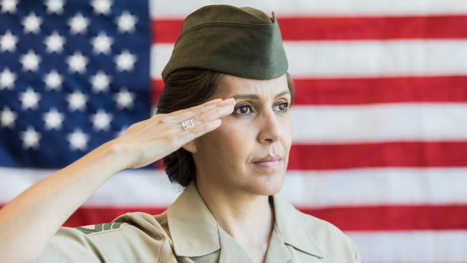 Serious mature Hispanic female military officer salutes the American flag.