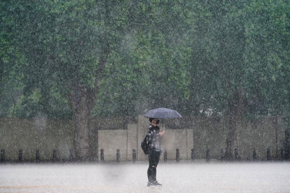 A woman stands in the rain in Horse Guards Parade, Westminster as heavy rain sweeps through central London. Thunderstorms bringing lightning and torrential rain to the south are set to continue until Monday, forecasters have said. Picture date: Sunday July 25, 2021. (PA Wire)