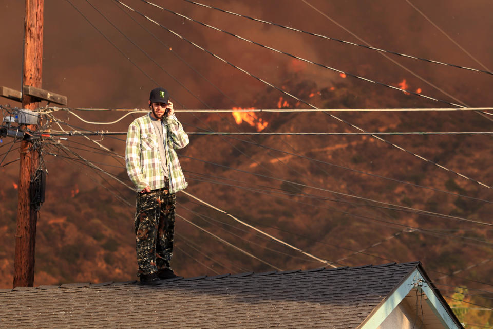 A resident on the roof of a house talks on the phone as a wildfire burns in the hills just north of the San Gabriel Valley community of Glendora, Calif., on Thursday, Jan 16, 2014. Southern California authorities have ordered the evacuation of homes at the edge of the fast-moving wildfire burning in the dangerously dry foothills of the San Gabriel Mountains. (AP Photo/Ringo H.W. Chiu)