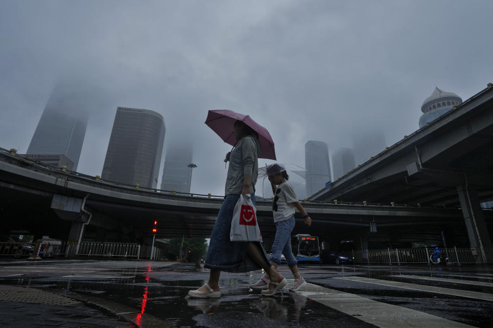 A woman and a child use umbrellas to protect themselves from rainfall brought about by tropical storm as they walk by Central Business District in Beijing, Tuesday, Aug. 1, 2023. Chinese state media report some have died and others are missing amid flooding in the mountains surrounding the capital Beijing. (AP Photo/Andy Wong)