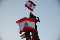 Demonstrators wave Lebanese national flags as they stand atop a statue on Martyrs' square during an anti-government protest in downtown Beirut