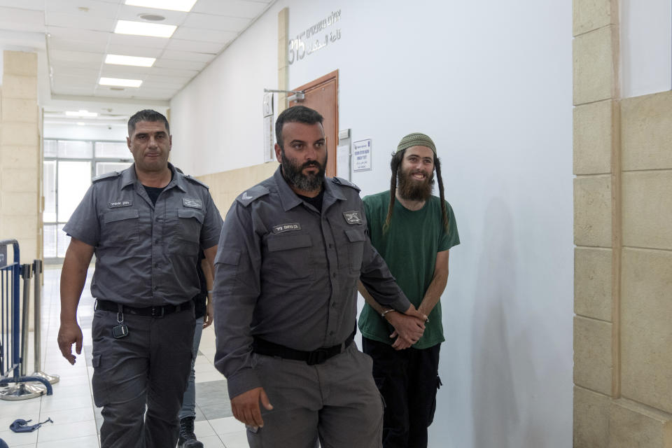 Elisha Yered, 22, right, is led handcuffed by officers during an appearance at the Jerusalem District Court on Tuesday, Aug. 8, 2023. Yered is one of two Israeli settlers arrested on suspicion of involvement in the killing of a Palestinian man in the West Bank on Friday. (AP Photo/Ohad Zwigenberg)