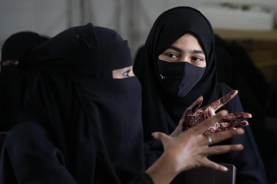A veiled Indian Muslim student, her hands decorated with henna, talks to her friend as they gather to meet student activists in Kundapur in district Udupi, Karnataka state, India, Saturday, Feb. 26, 2022. Muslim students in this southern Indian state have found themselves at the center of a debate over hijab bans in schools. In question is the place of Islamic head coverings in the Hindu-majority but constitutionally secular nation. (AP Photo/Aijaz Rahi)