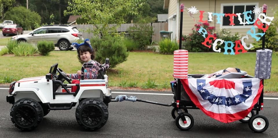 In a remote control car driven by her father Trenton Reynolds, 3-year-old Tegan sits in the driver's seat while brother Caleb naps in the wagon being pulled behind as they take part in the Marine Drive Fourth of July Parade on Monday.