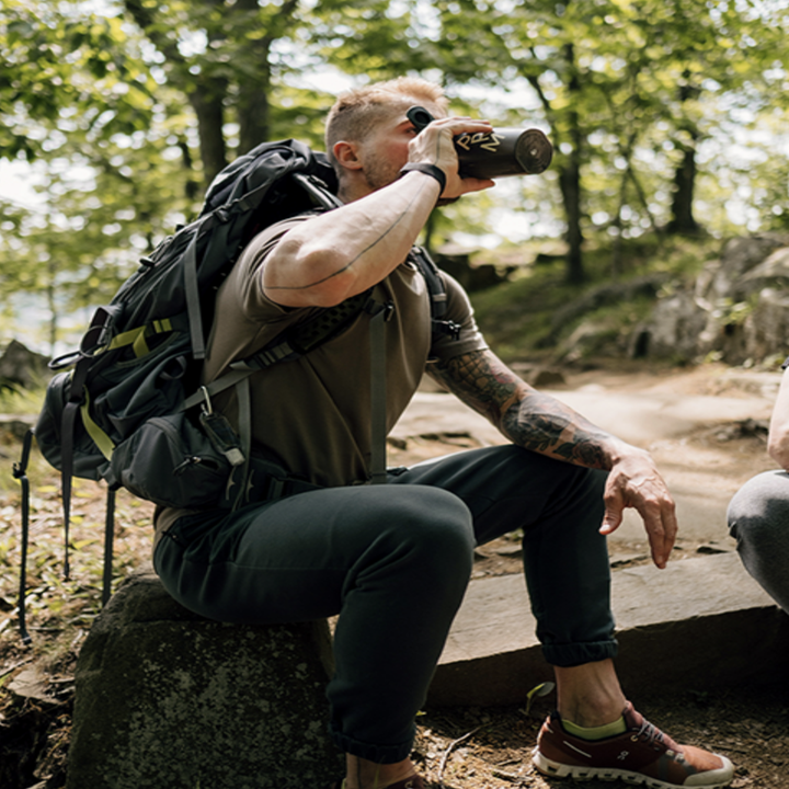 Someone drinking from their protein mixer while hiking on a trail