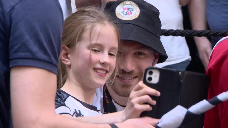 A young girl takes a selfie of her and a Bromley FC player during a meet and greet event