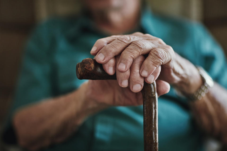Close-up of elderly person's hands resting on a cane, symbolizing retirement or aging