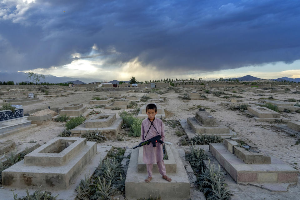 An Afghan boy poses for a photo with his toy gun on a grave as he spend his time at a cemetery in Kabul, Afghanistan, Thursday, May 5, 2022. There are cemeteries all over Afghanistan's capital, Kabul, many of them filled with the dead from the country's decades of war. They are incorporated casually into Afghans' lives. They provide open spaces where children play football or cricket or fly kites, where adults hang out, smoking, talking and joking, since there are few public parks. (AP Photo/Ebrahim Noroozi)