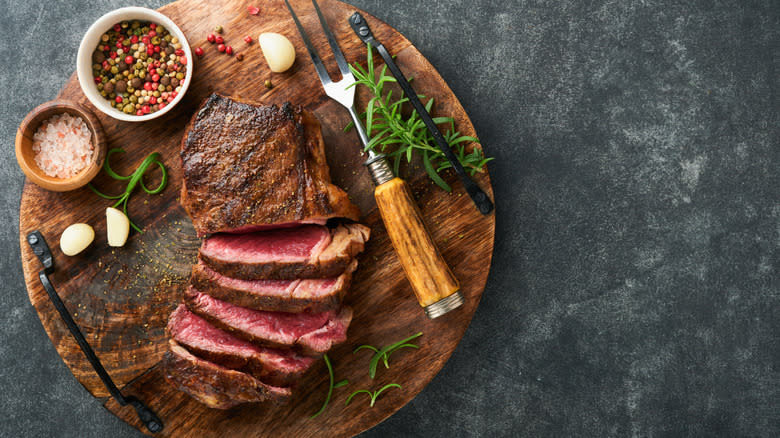 A board of steak, a fork, garlic cloves, and condiments