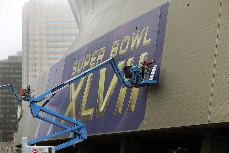 In this Jan. 15, 2013, photo, workers put up signage for the upcoming Super Bowl on the Superdome in New Orleans. With the Super Bowl in New Orleans Feb. 3 and Mardi Gras falling just nine days later, the city is gearing up for a massive celebration and influx of tourists that locals are calling "Super Gras." (AP Photo/Gerald Herbert)