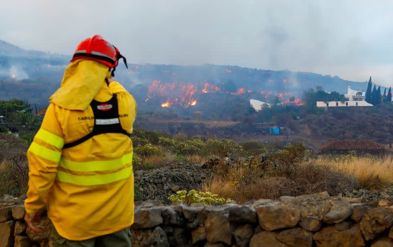 A forest firefighter watches as lava flows next to houses following the eruption of a volcano in Spain