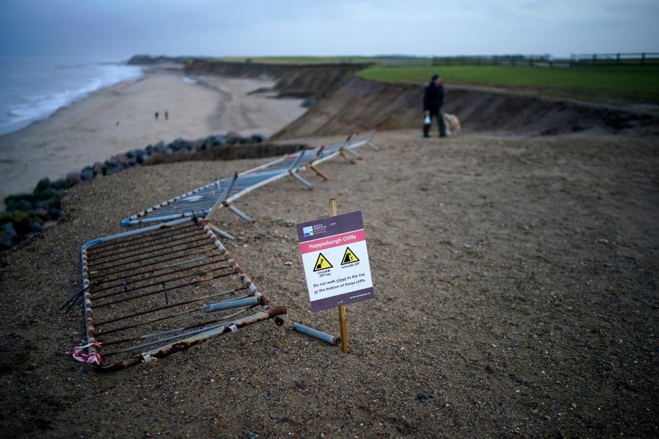 People walk past a recent landslip on the cliff edge and beach