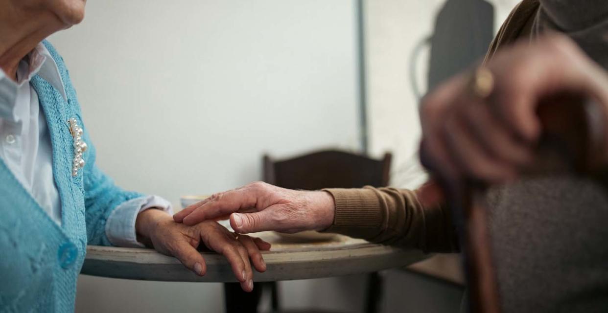 The hands of a male and female couple wearing cardigans in a retirement community.