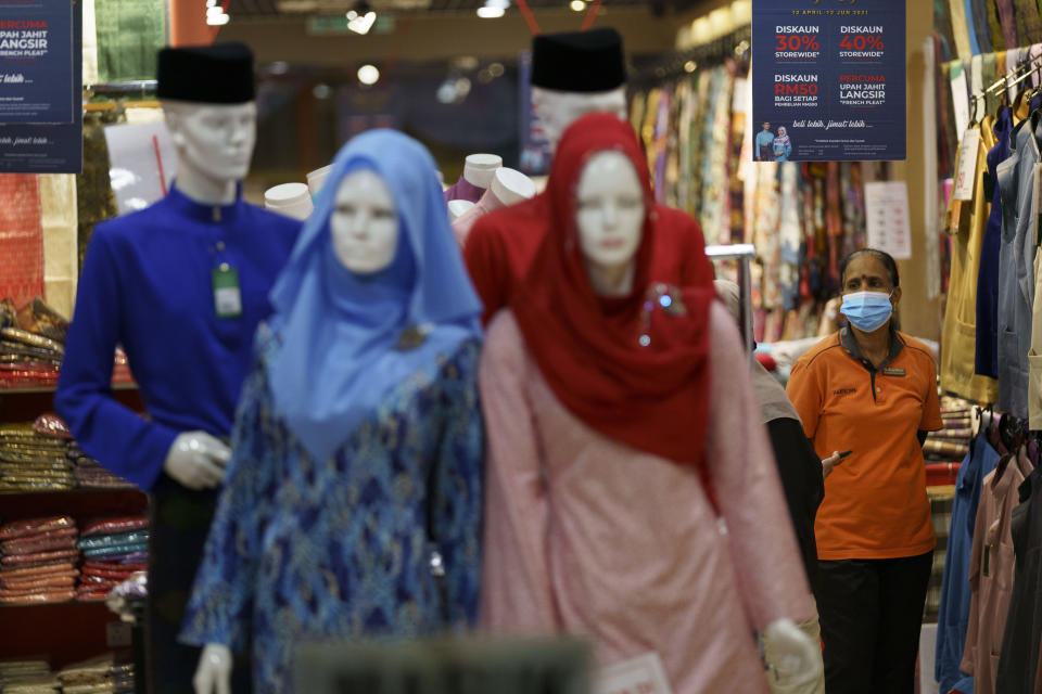 In this Saturday, April 24, 2021, photo, a clothing shop clerk wearing a protective mask waits for customers at the Ramadan bazaar in Kuala Lumpur, Malaysia. Malaysian Prime Minister Muhyiddin Yassin announced Monday that the whole country will be placed under a near lockdown for about a month but all economic sectors will be allowed to operate. (AP Photo/Vincent Thian)