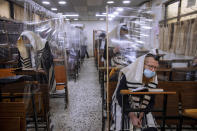 FILE - In this Monday, Sept 21, 2020 file photo, ultra-Orthodox Jews wear face masks during a morning prayer in a synagogue separated by plastic partitions, in Bnei Brak, Israel. For Israel's ultra-Orthodox Jews, coronavirus restrictions have raised numerous questions about how to maintain their religious lifestyle during the outbreak. A religious publisher in Jerusalem released a book in July with over 600 pages of guidance from 46 different rabbis. (AP Photo/Oded Balilty, File)