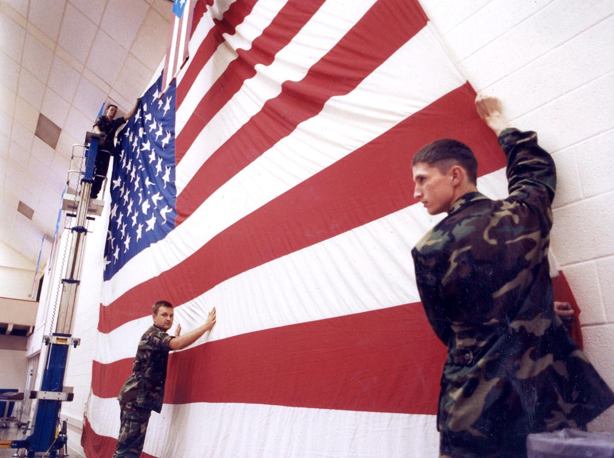 Airman Basic Jonathan Tucker (right) assists Airman Basic Lance Watson (lower left) and Airman Richard Furner (on the lift) with hanging an American flag at the then-named Abilene Civic Center in preparation for the World’s Largest Barbecue in 1991.