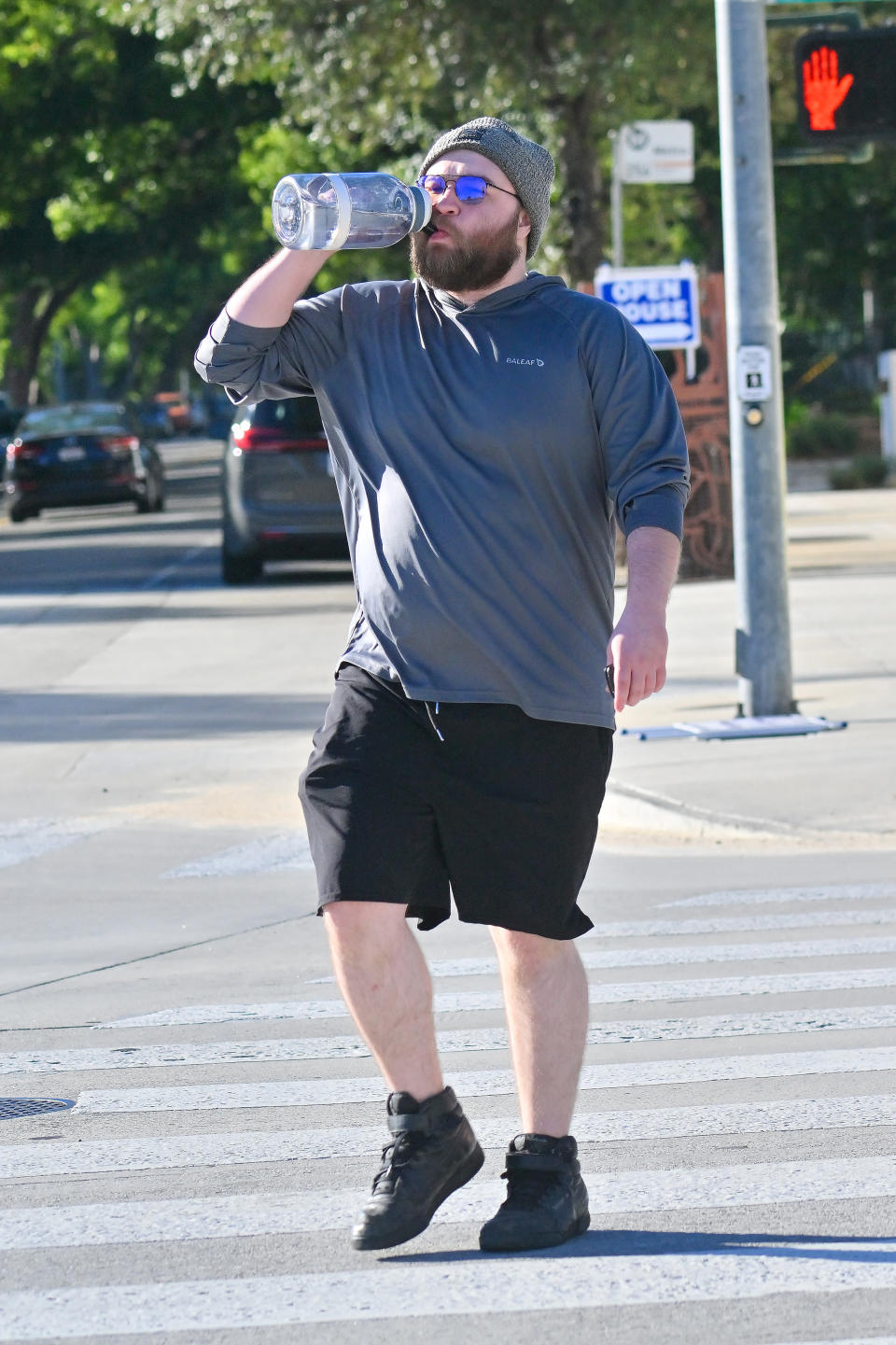 Angus T. Jones sips on water bottle while wearing sweatshirt, shorts and hat