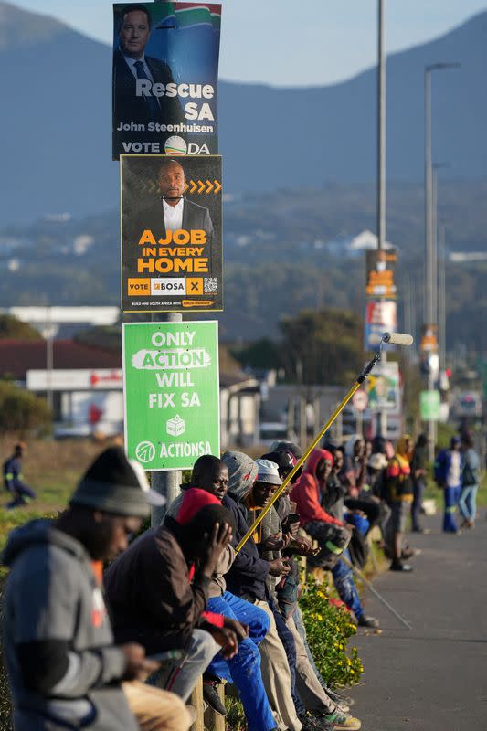 FILE PHOTO: Job seekers sit beneath campaign posters for the South African general elections, in Cape Town