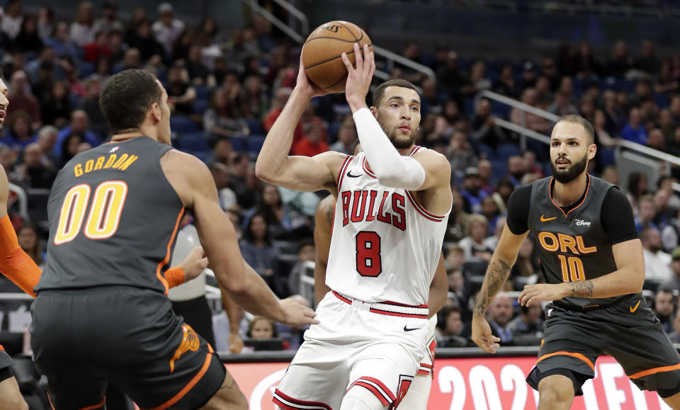 Chicago Bulls guard Zach LaVine (8) passes the ball as he gets between Orlando Magic forward Aaron Gordon (00) and guard Evan Fournier, right, during the first half of an NBA basketball game, Monday, Dec. 23, 2019, in Orlando, Fla. (AP Photo/John Raoux)