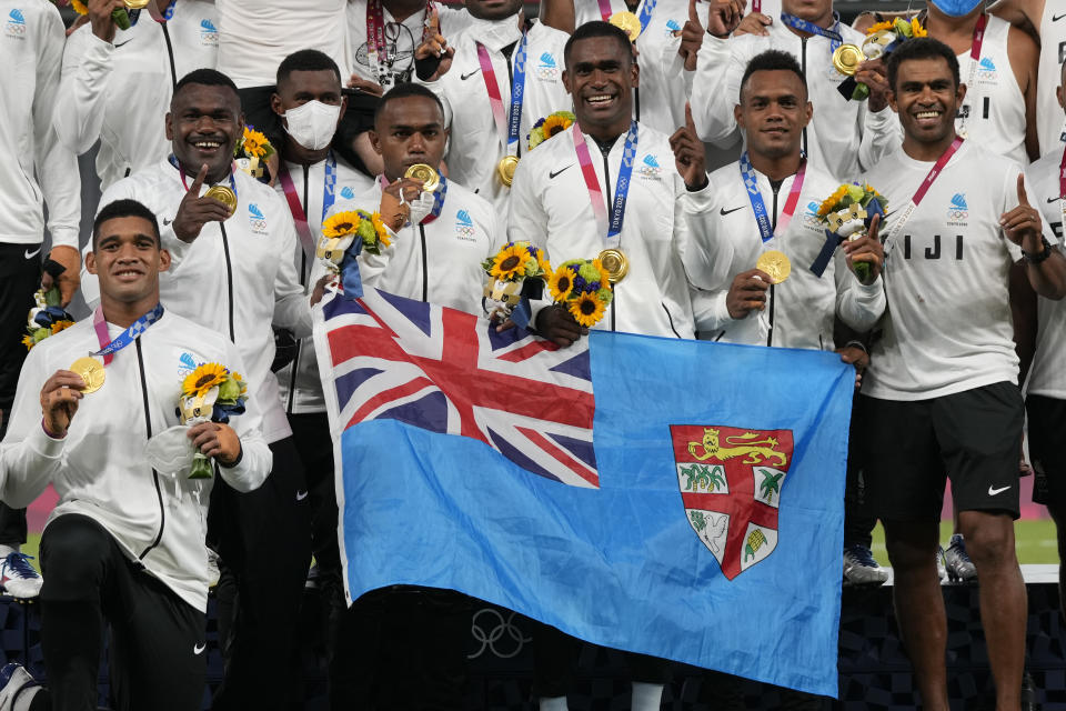 Member's of Fiji's team and staff hold a national flag, as they pose with their gold medals in men's rugby sevens at the 2020 Summer Olympics, Wednesday, July 28, 2021 in Tokyo, Japan. (AP Photo/Shuji Kajiyama)