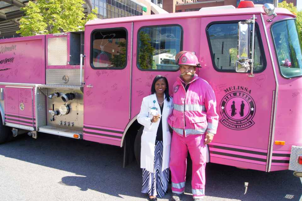 Dr. Erica Stringer-Reasor stands next to a firefighter in front of a pink fire truck with a "pink heals" emblem painted on the door..