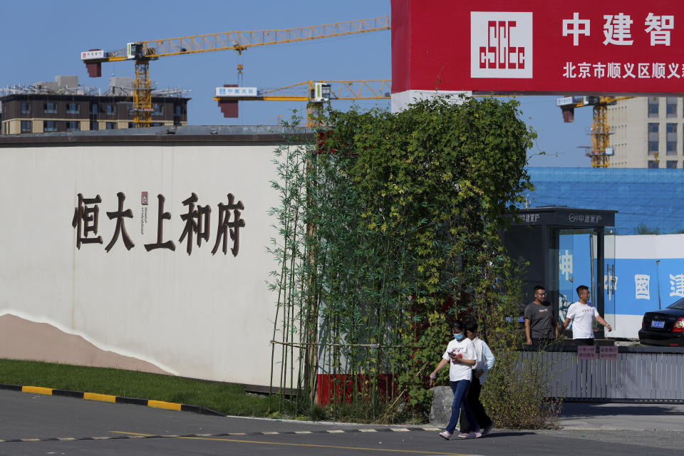 People walk out from an Evergrande new housing development in Beijing, Wednesday, Sept. 22, 2021. The Chinese real estate developer whose struggle to avoid defaulting on billions of dollars of debt has rattled global markets announced Wednesday it will make a closely watched interest payment due this week, while the government was silent on whether it might intervene. (AP Photo/Andy Wong)