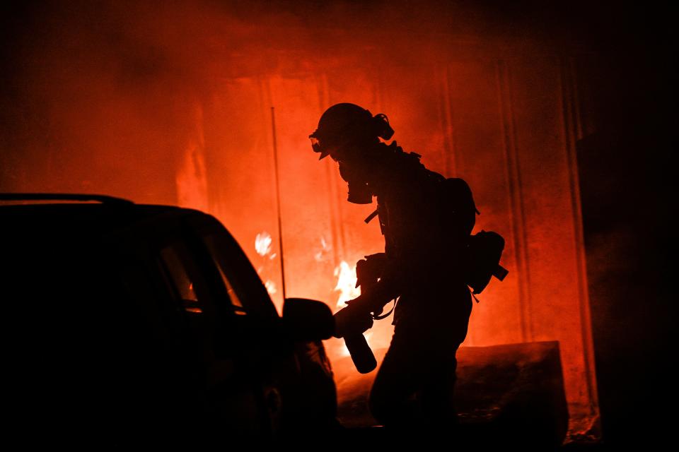 A photojournalist walks among the flames of a wildfire in rural Aguanga on Monday. (The Orange County Register via AP)